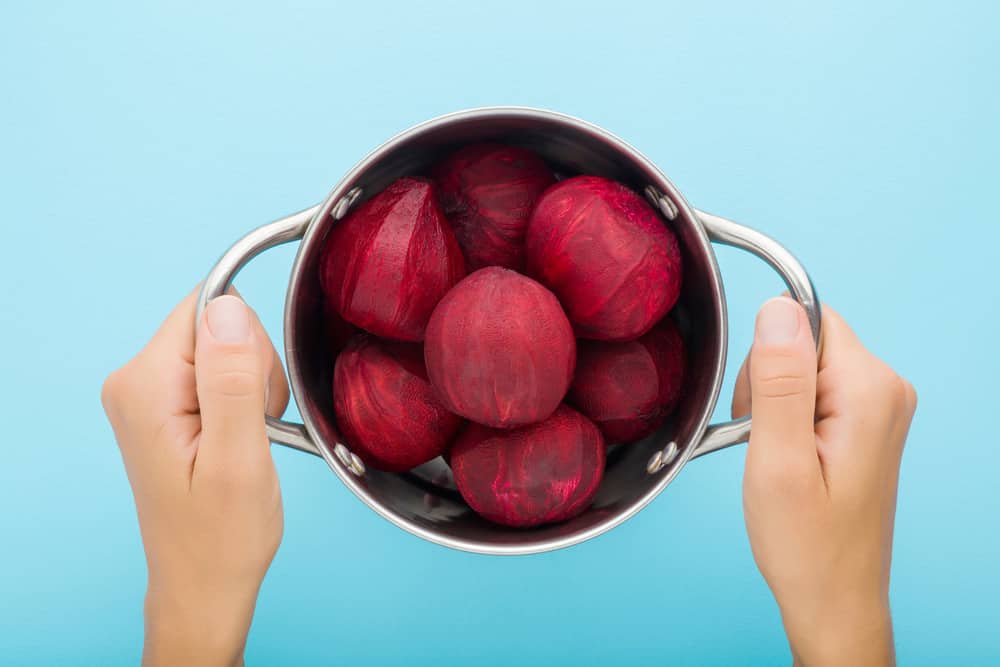 woman hands holding steel saucepan with dark red peeled boiled beets