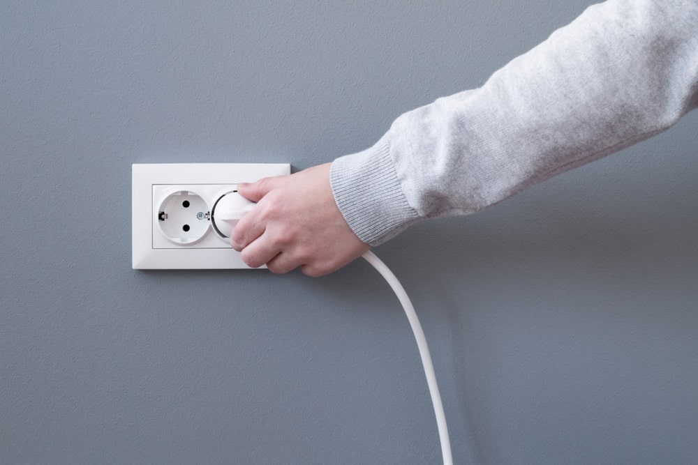 Hand plugging in an electric cord into a white plastic socket
