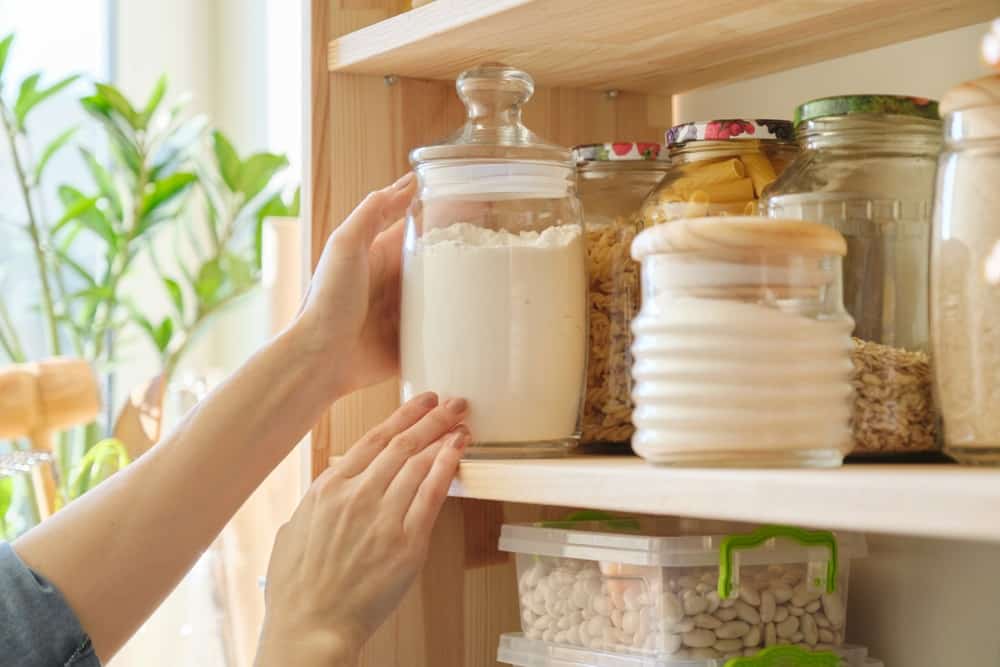 hands placing flour on a pantry shelf in air tight jar