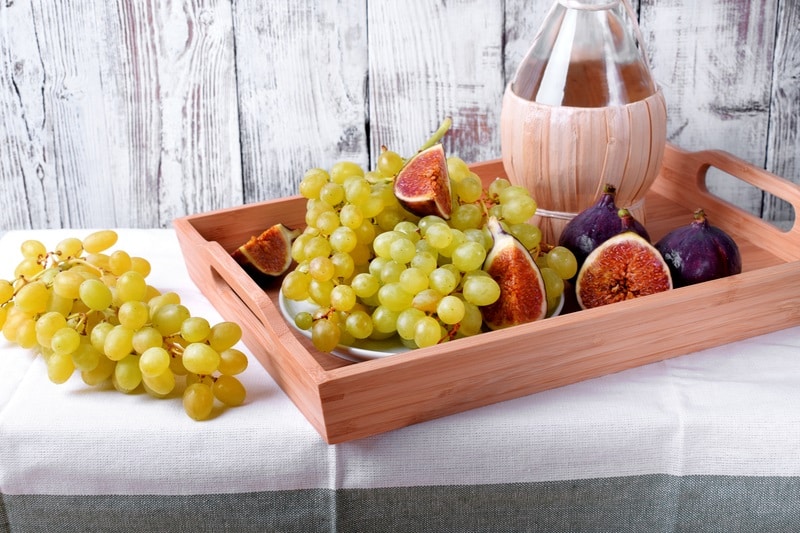 White grapes, figs and Italian spirit Grappa on wooden tray