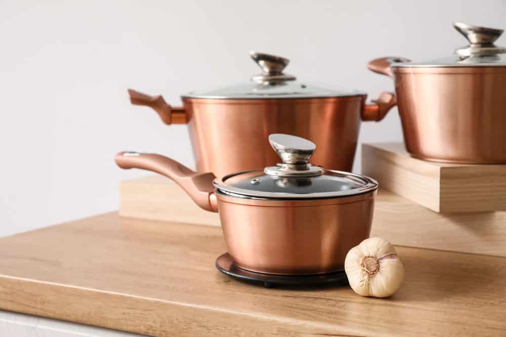 Copper saucepan with garlic on counter near light wall