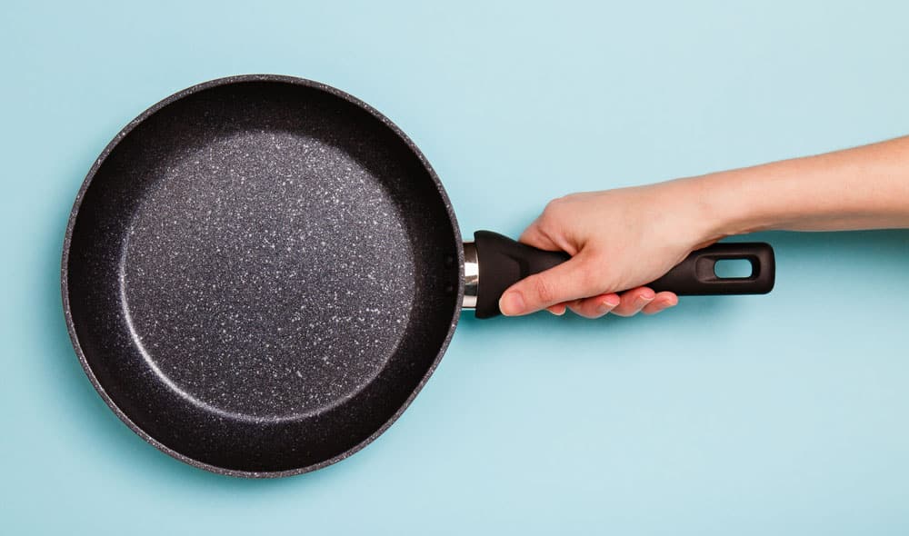 frying pan in woman's hand on blue background