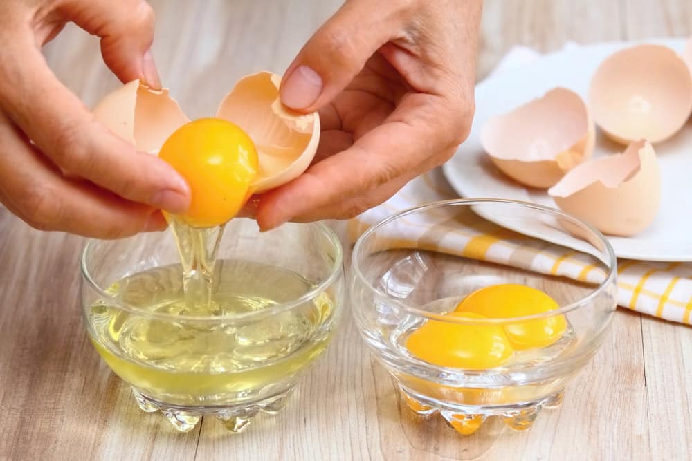 Woman hands breaking an egg to separate egg white and yolks