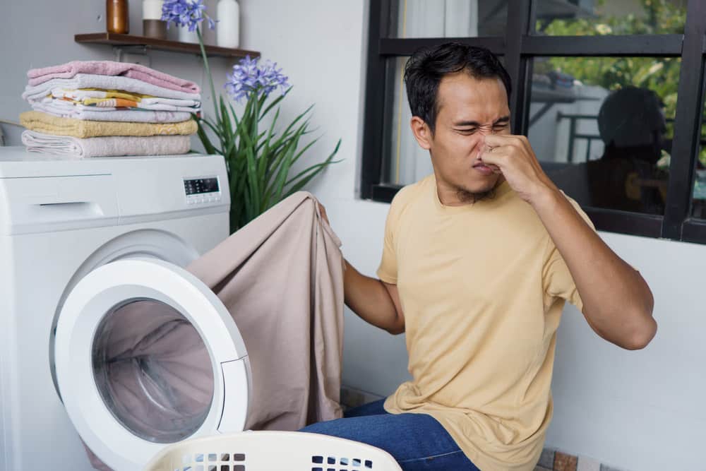 Man doing laundry at home loading clothes into washing machine bad odor