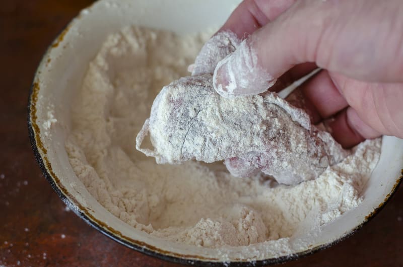 man's hand pours piece raw fish flour