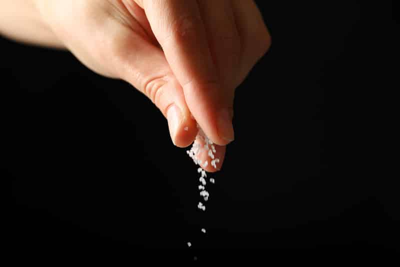 female hand adding salt black background