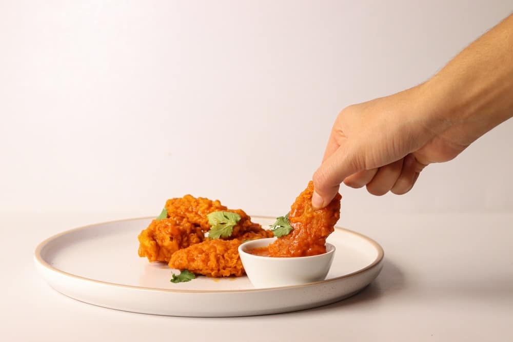 holding buffalo wing with red hot sauce