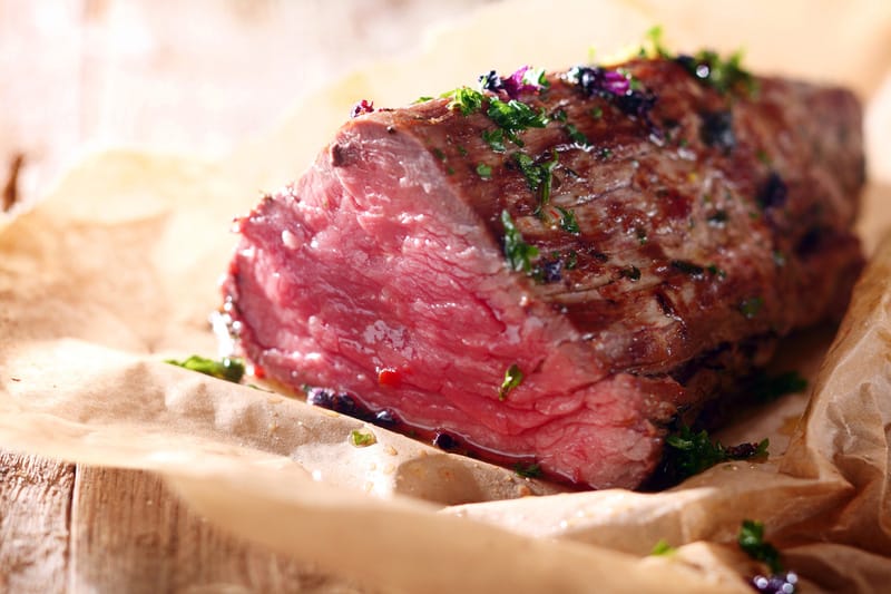 Tender lean rare roast beef seasoned with fresh herbs and spices on a piece of oven paper