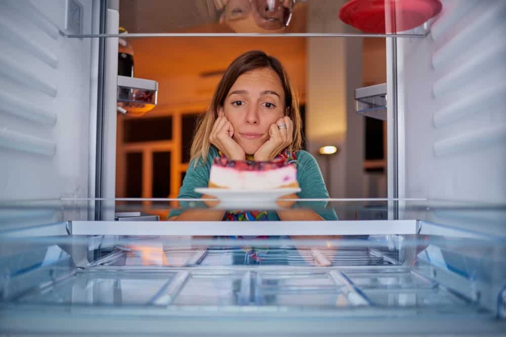 Woman looking at cheesecake in fridge