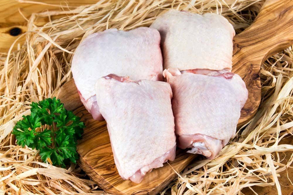 Raw Chicken Thighs on cutting board and straw.