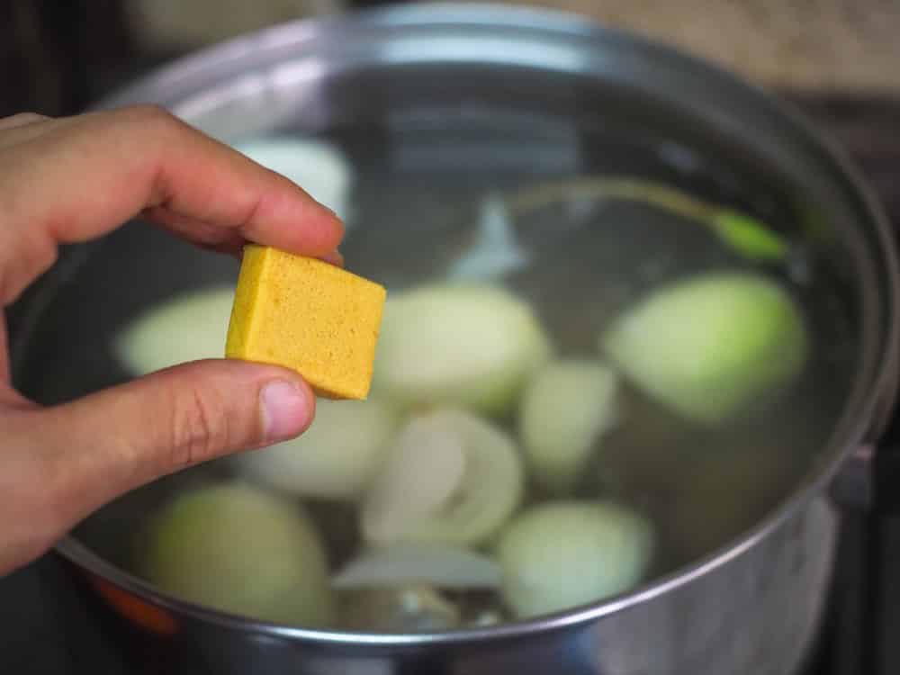 Bouillon, stock or broth cubes in female hand with a pot of soup