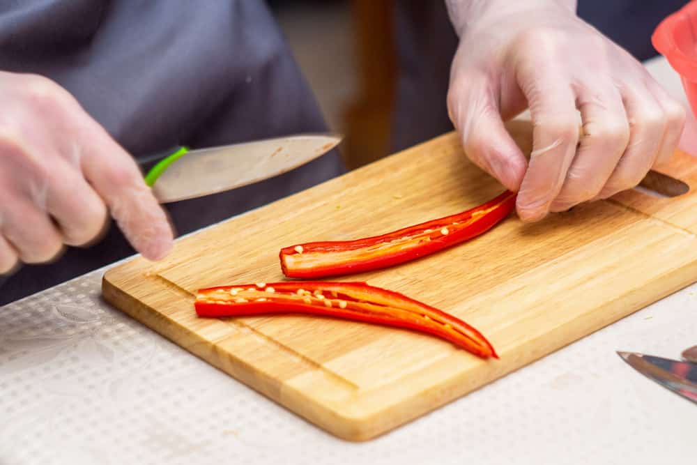 Chef wearing gloves with a sharp knife and clean cuts red chili peppers