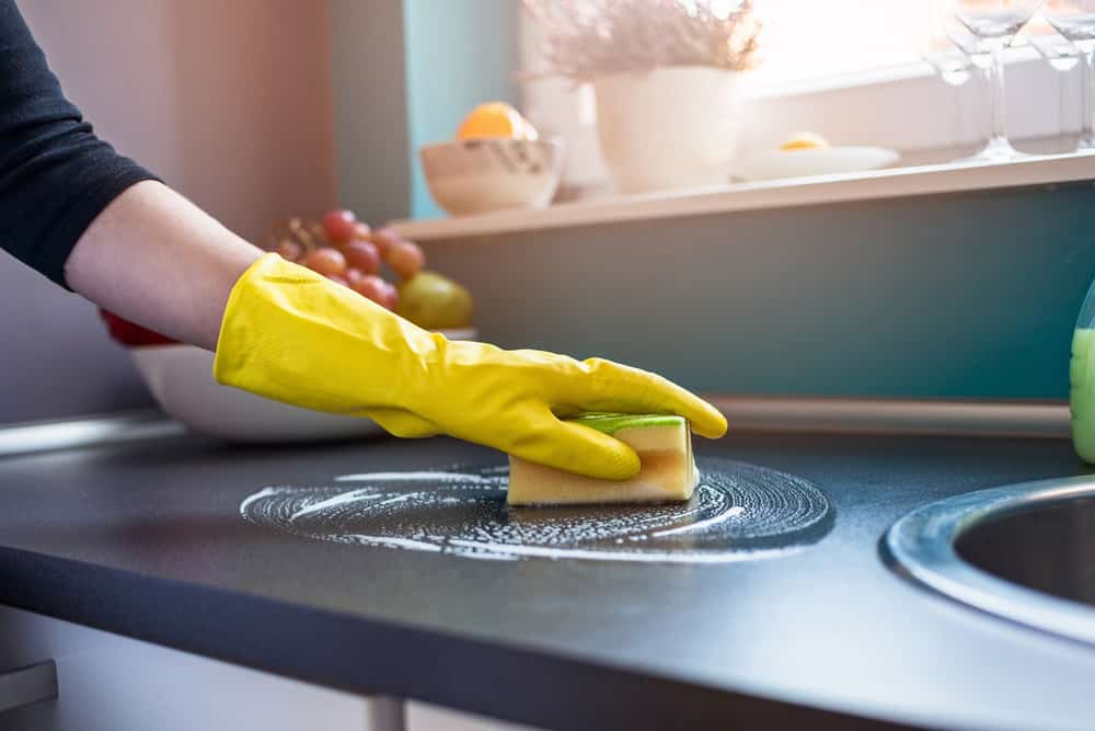 Woman's hands in yellow rubber gloves cleaning kitchen 