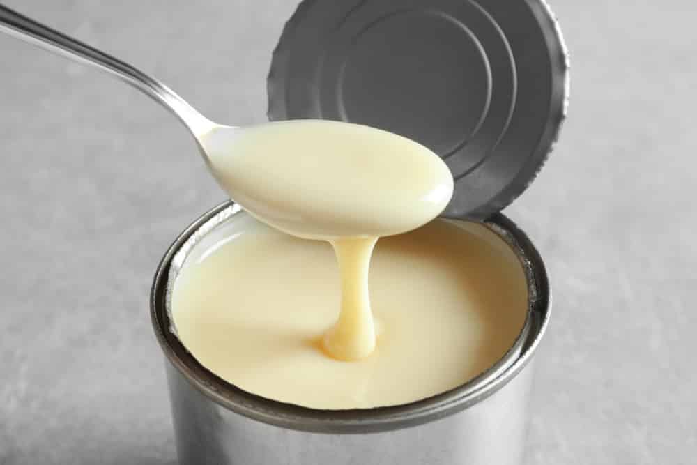 Condensed milk pouring from spoon into tin can