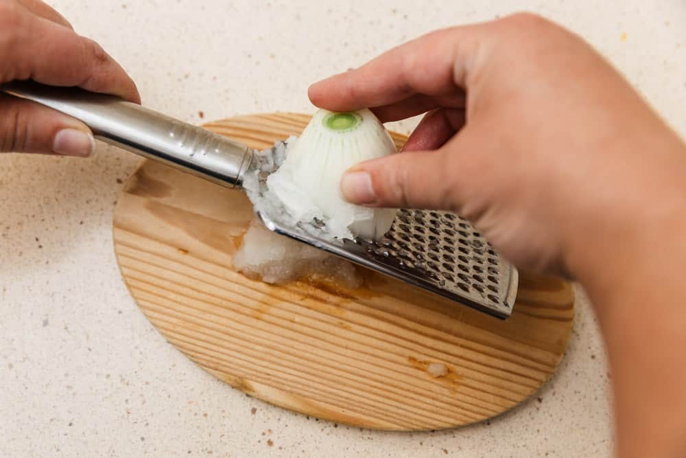 Female cook's hands are grating an onion on a metal grater