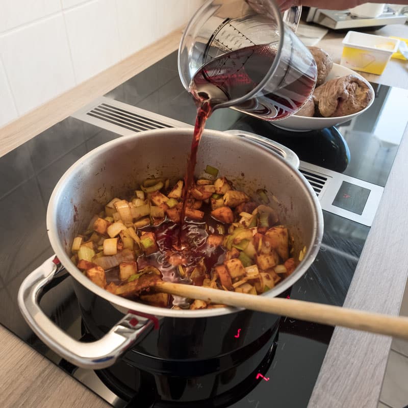 female hand pouring red wine roasting vegetable