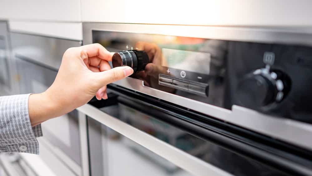 Male hand turning temperature knob of modern oven