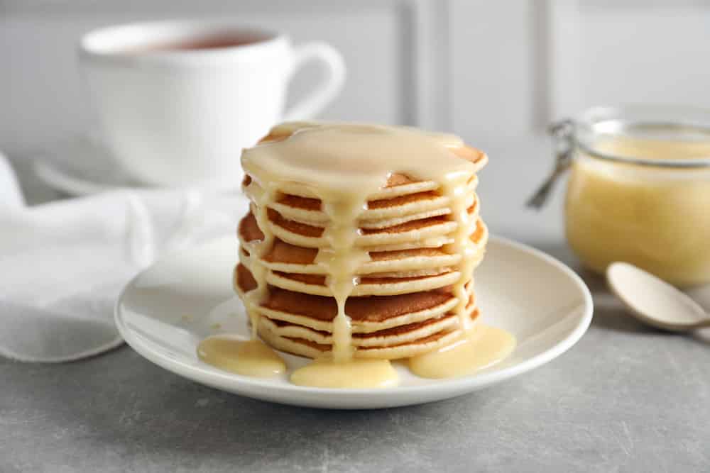 Plate with pancakes and condensed milk served on table