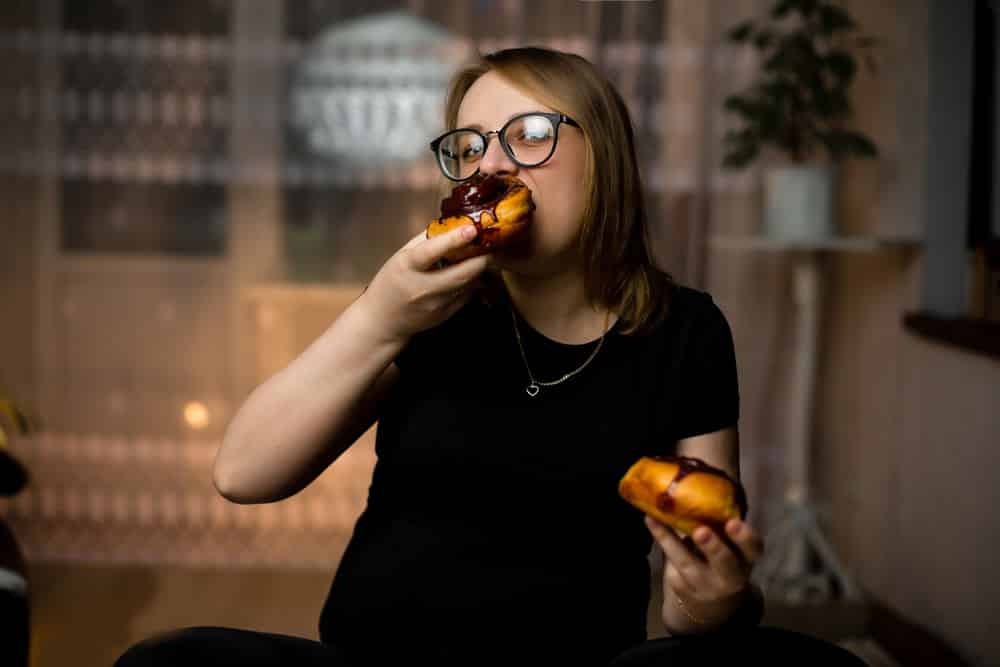 A pregnant girl is sitting and eating fresh cinnamon rolls