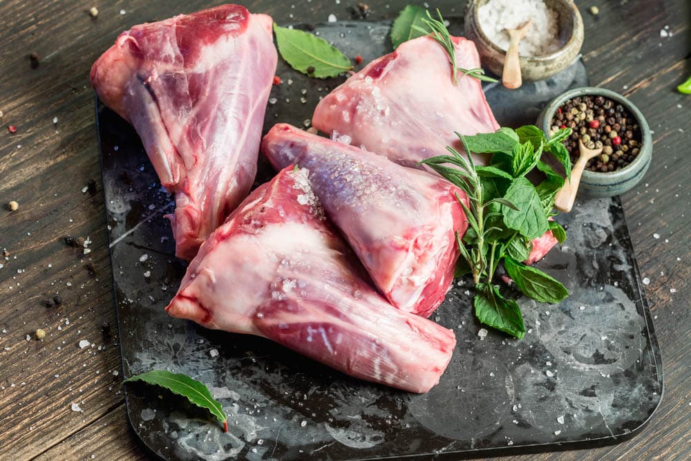 Raw lamb shanks with salt and pepper on stone tray