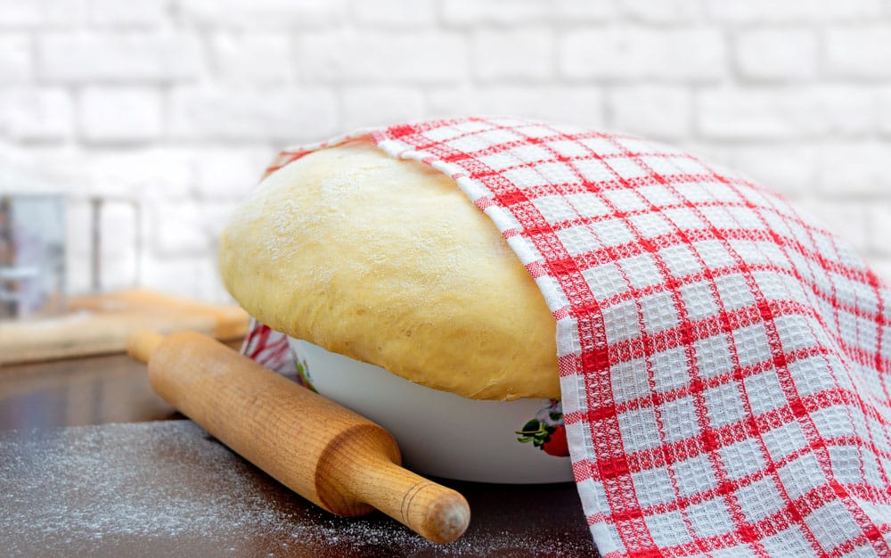 Raw yeast dough covered with a towel in a bowl