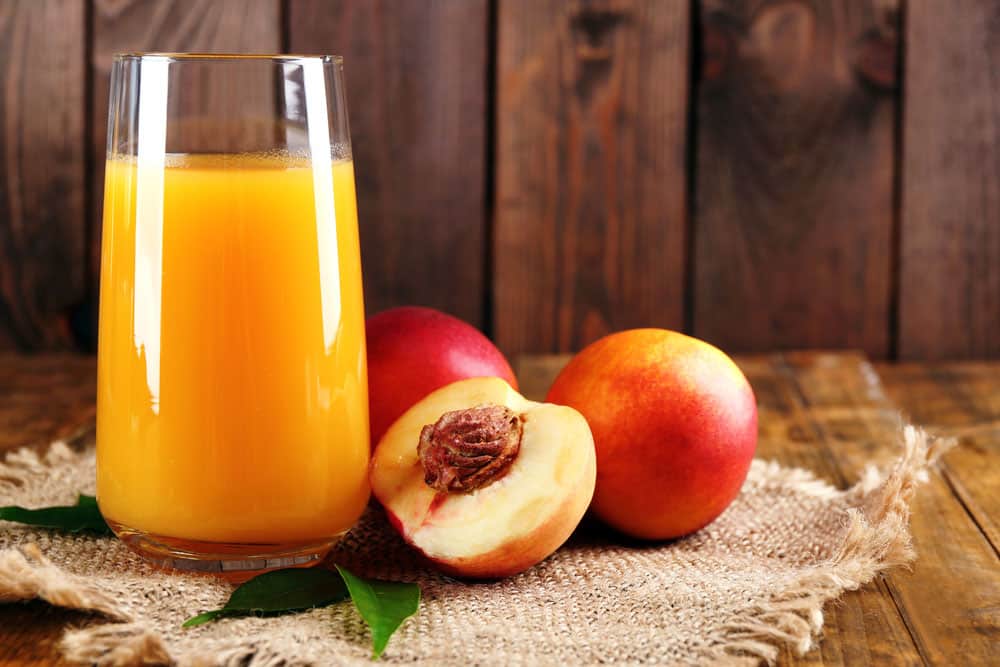 Ripe peaches and glass of juice on wooden