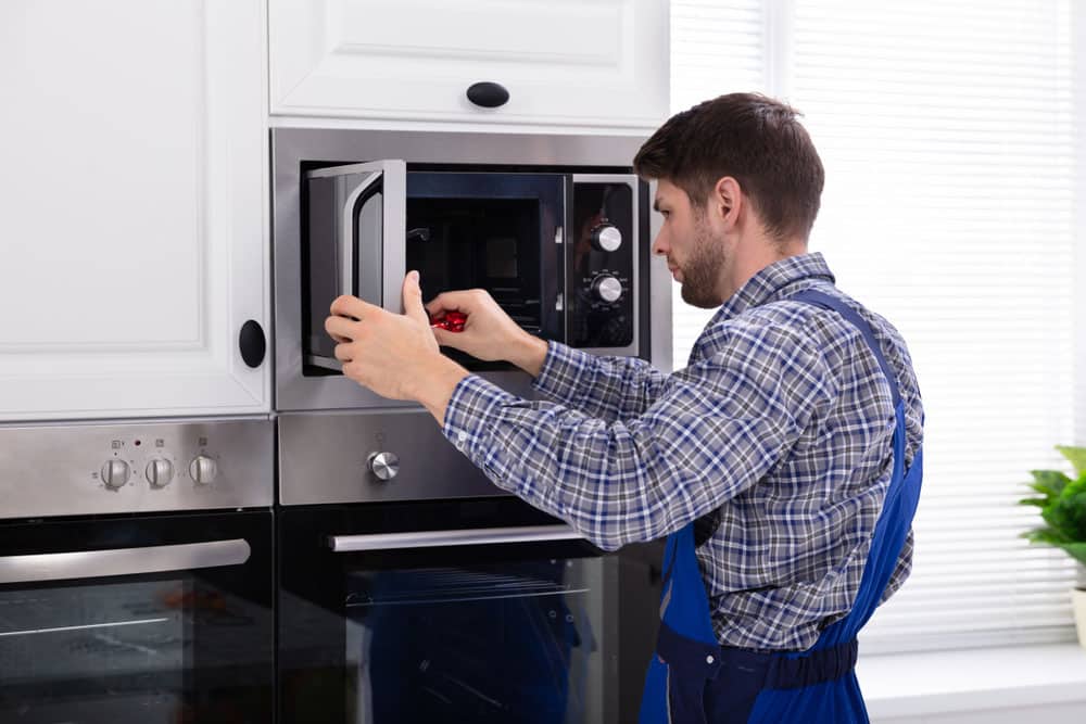 Side View Of Young Man Repairing Microwave Oven In Kitchen