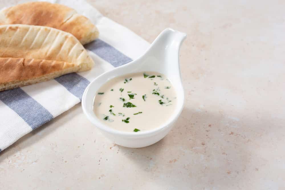 A view of a tahini sauce in a spoon shaped condiment cup