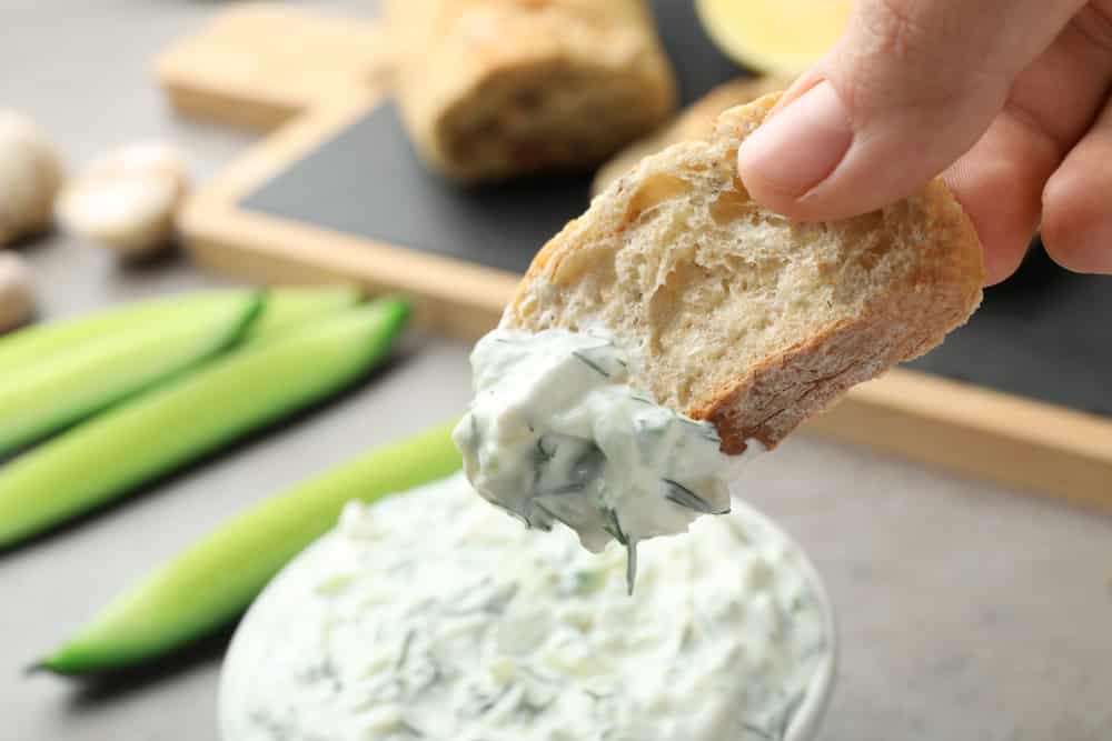 Woman dipping bread in Traditional Tzatziki