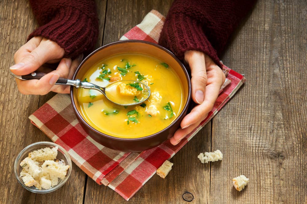 Woman hands holding bowl of vegetable soup with parsley and croutons 