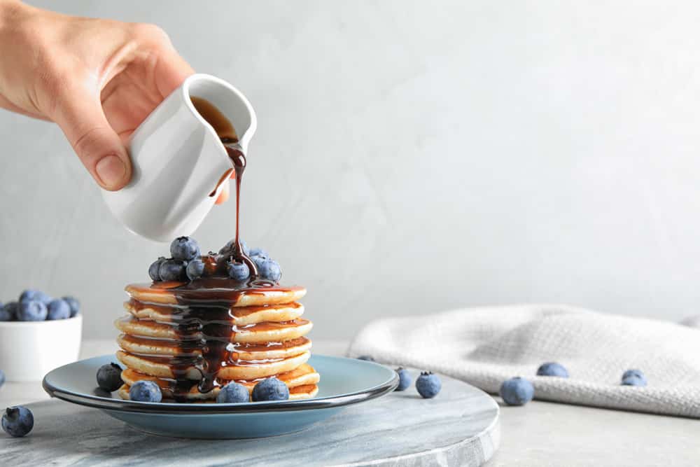 Woman pouring chocolate syrup onto fresh pancakes