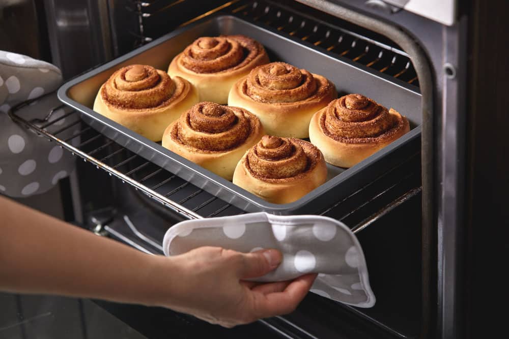 A woman takes out fresh buns from the oven