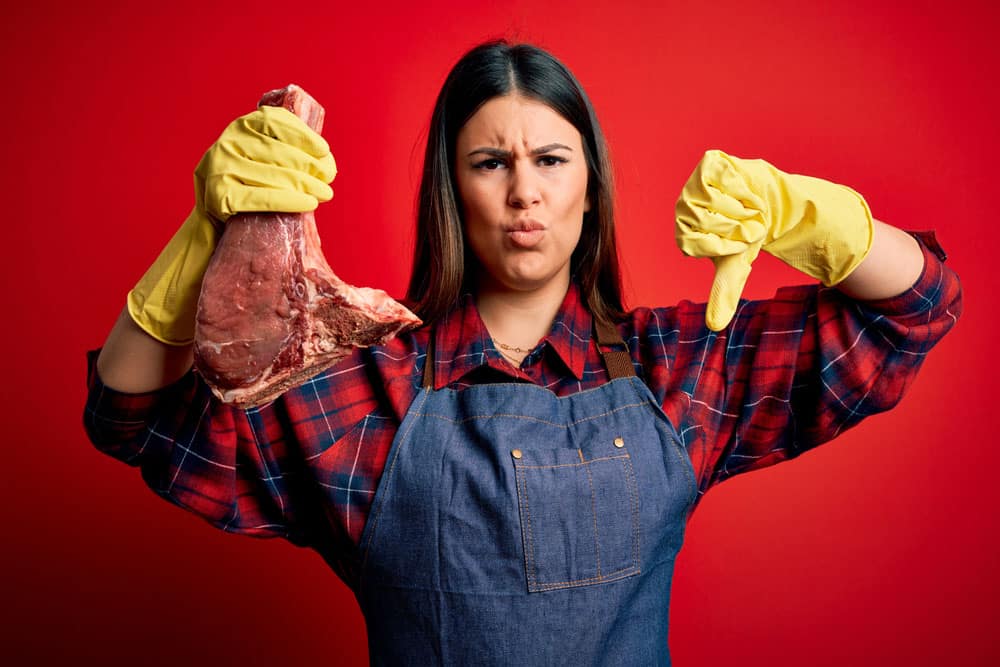 Young butcher woman holding fresh raw beef meat stake 