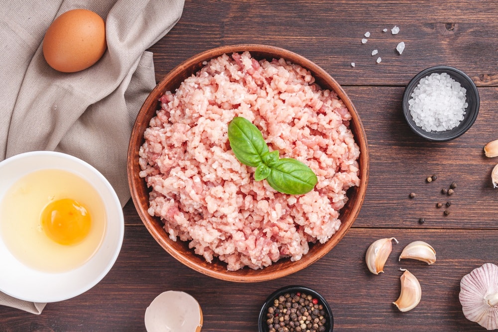 Raw minced meat in bowl on wooden table and ingredients