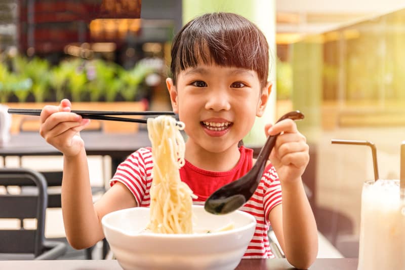 Asian little Chinese girl eating noodles soup