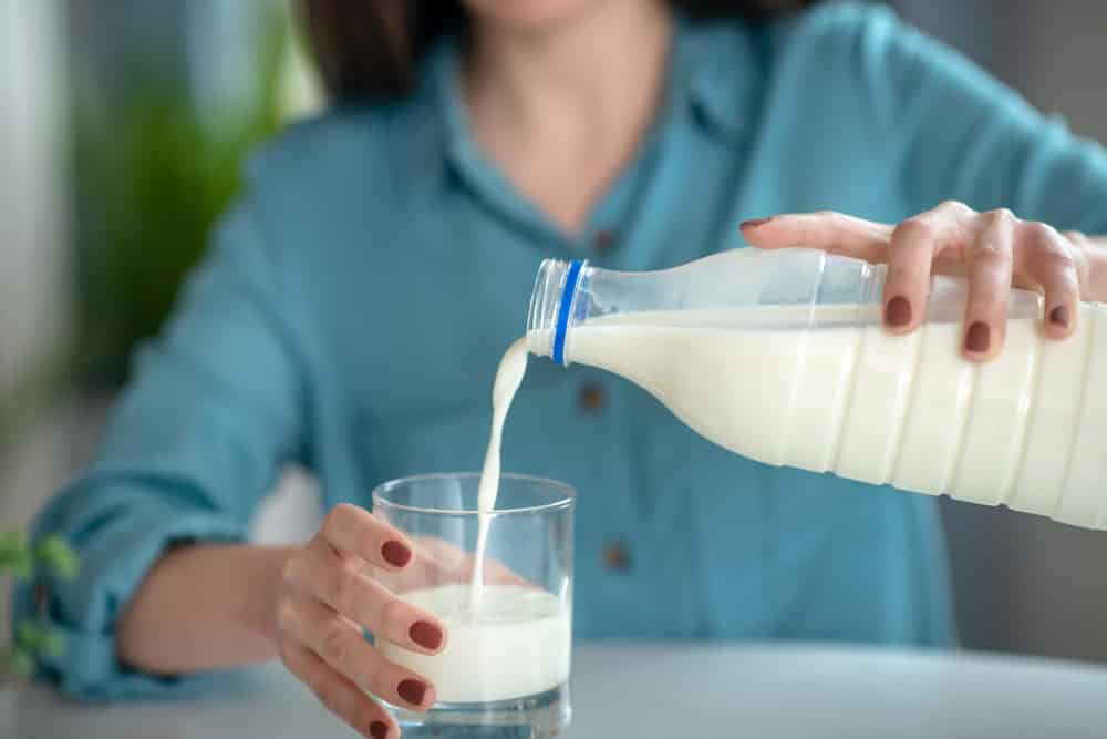 A woman pouring milk from the bottle to the glass