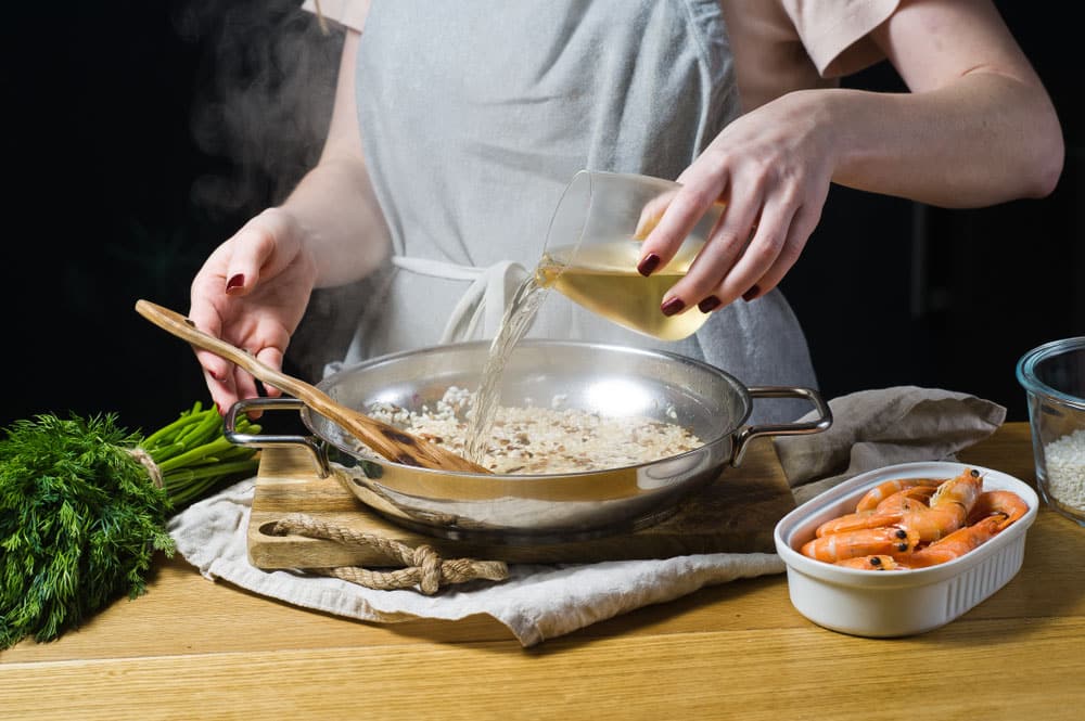 The chef pours white cooking wine into an Italian risotto