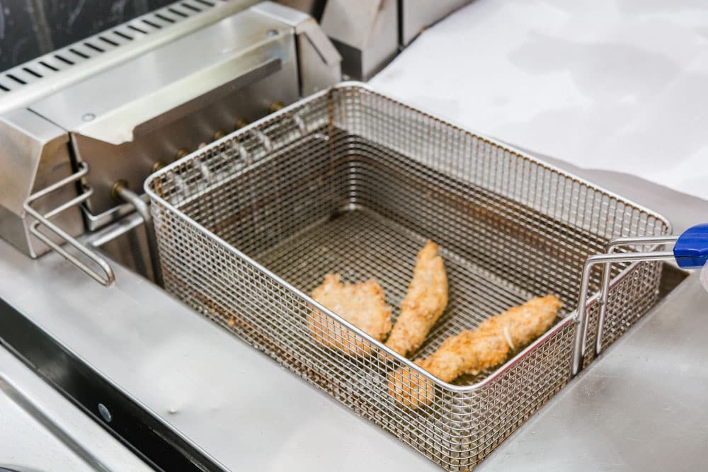 The cook fries meat in a deep fryer