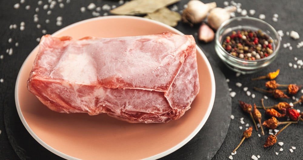 Frozen piece of raw meat on plate on black table