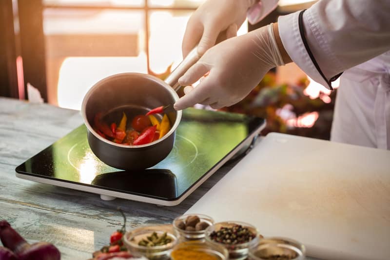 hand glove holding saucepan slices colorful spicy peppers