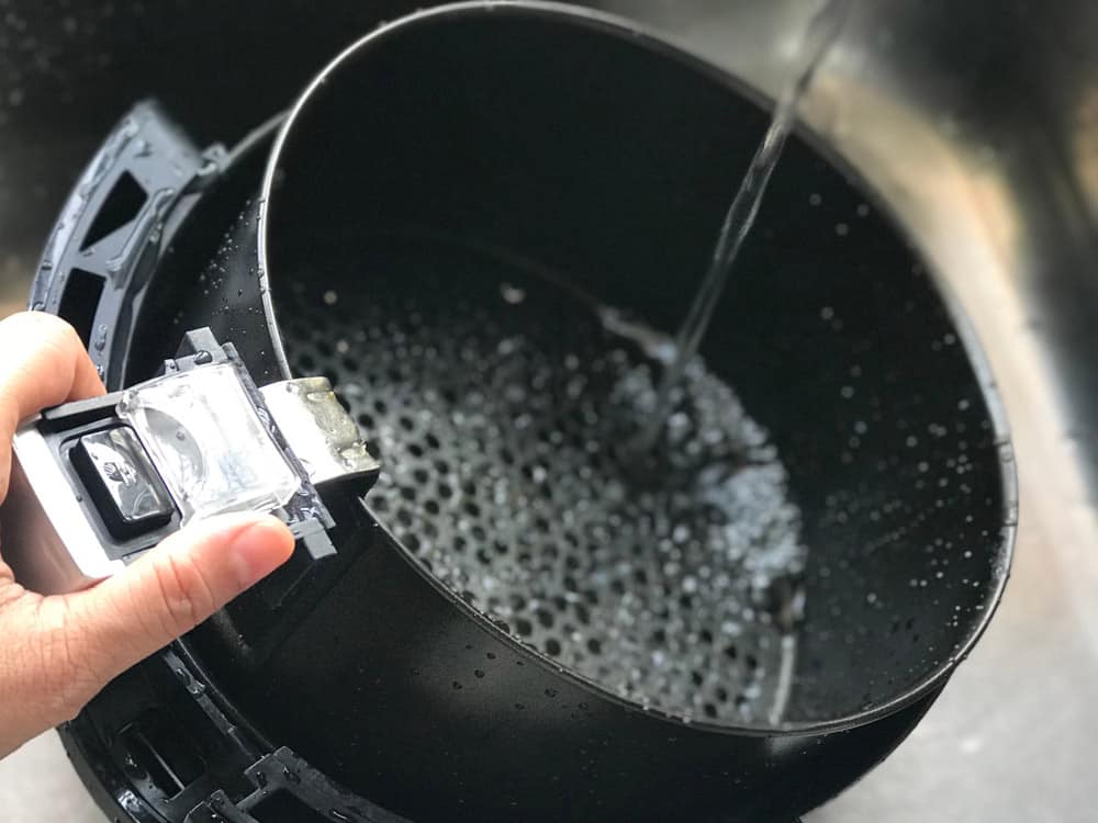 Women’s hand holding the handle air fryer’s basket for washing