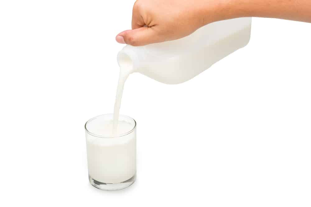 Hand holding fresh milk in a plastic gallon while pouring into the glass