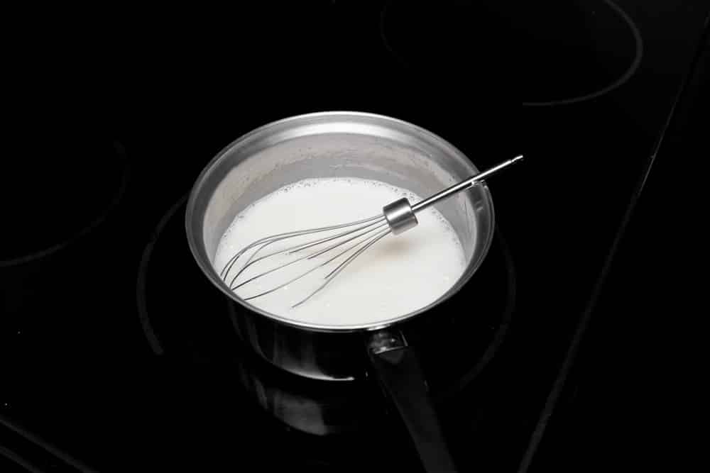metal whisk in a small metal pan with heavy cream being stirred