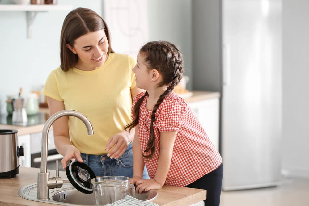 Mother and little daughter cleaning blender in kitchen