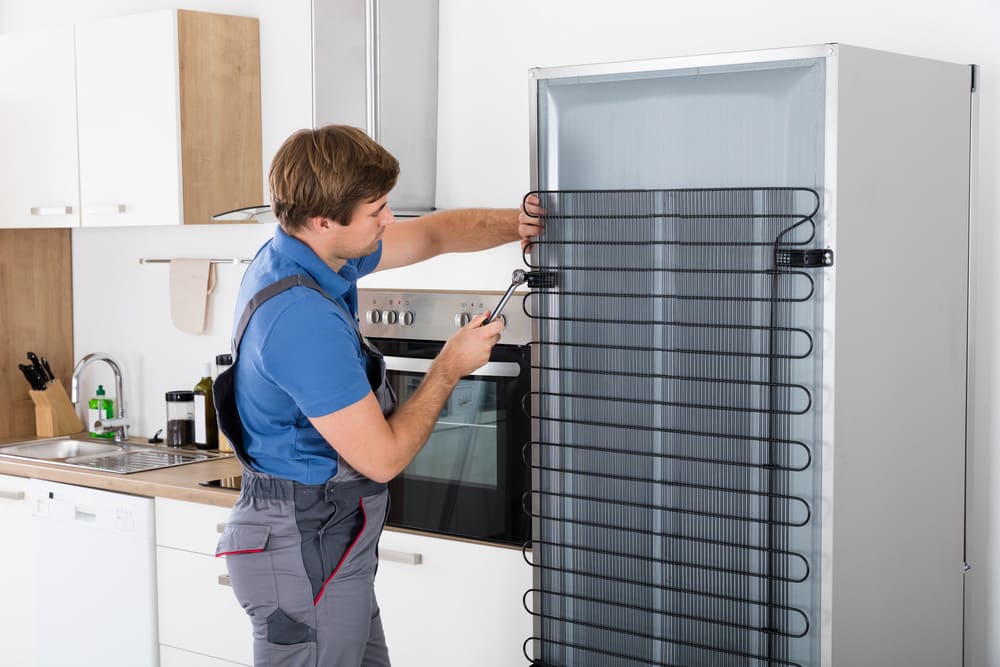 Serviceman In Overall Working On Fridge in Kitchen