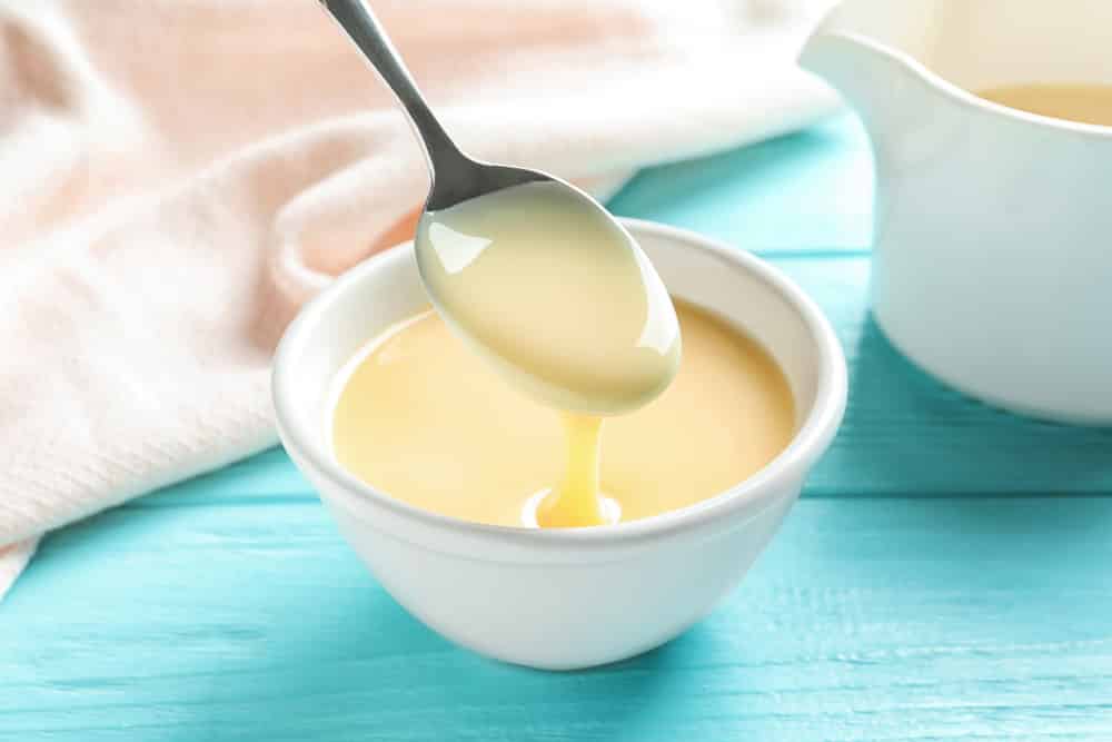 Spoon of pouring condensed milk over bowl on table