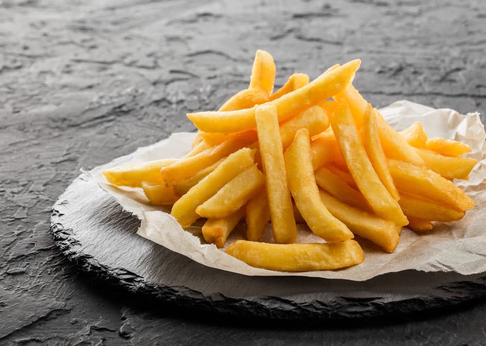 Tasty french fries potatoes on paper over black stone background.