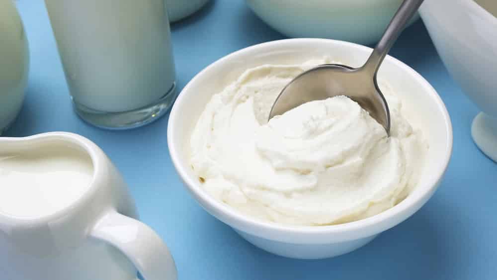 Whipped cream with spoon on blue background, Greek yogurt