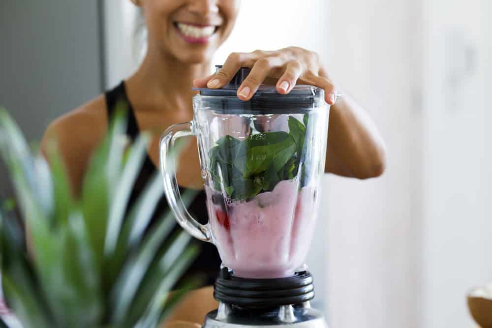 Woman blending spinach, berries, bananas and almond
