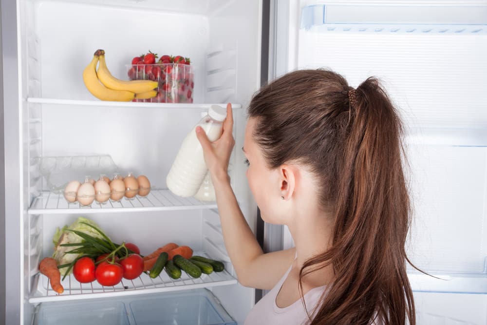 Woman chosen milk in opened refrigerator